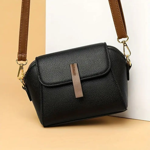 Dark small crossbody bag with front flap, textured finish, and brown strap
