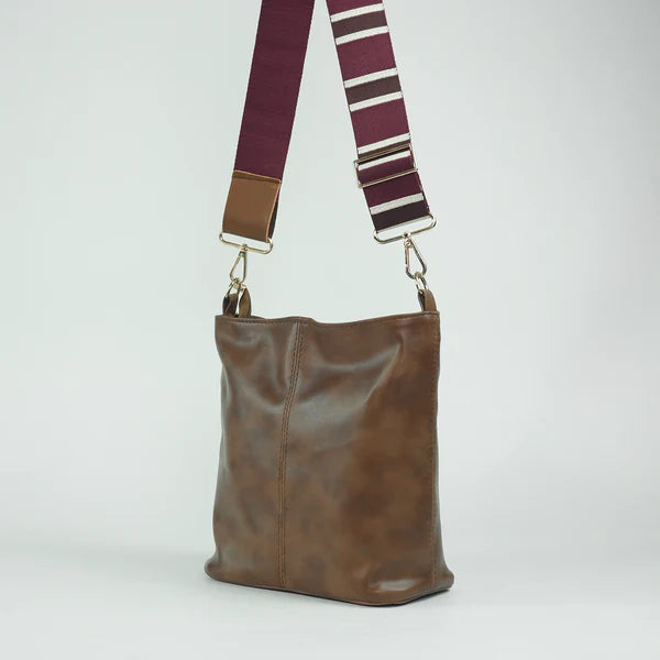 Brown leather tote bag with two top handles and striped adjustable shoulder strap