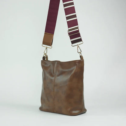 Brown leather tote bag with two top handles and striped adjustable shoulder strap