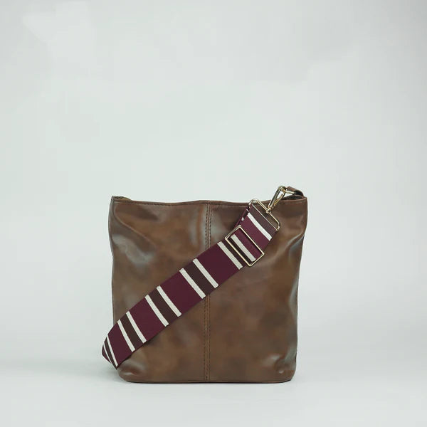 Brown leather bucket tote bag with diagonal striped crossbody strap and metal buckle
